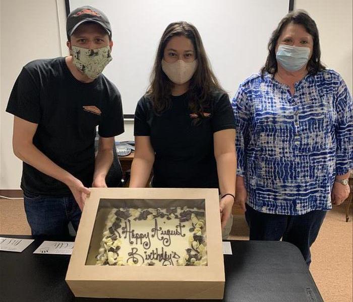 three employees wearing masks holding a birthday cake