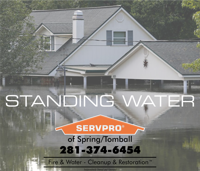 House in background with flood water almost up to roof, "standing water" towards middle and servpro logo under it